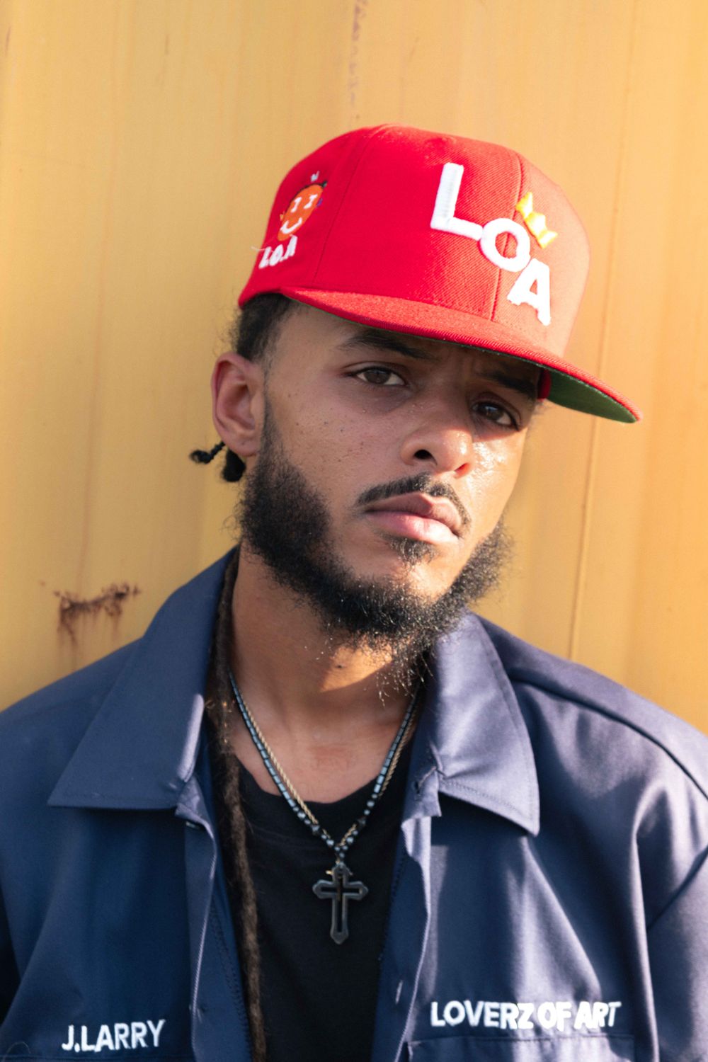 Musician in a red cap and navy work shirt against a yellow shipping container