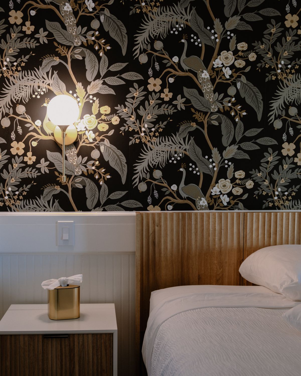 Guest room at The Gibson Inn with botanical wallpaper, a wall sconce and a white bed
