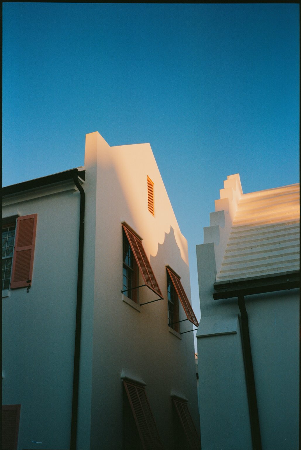 White stucco gables with coral Bermuda shutters against a deep blue sky